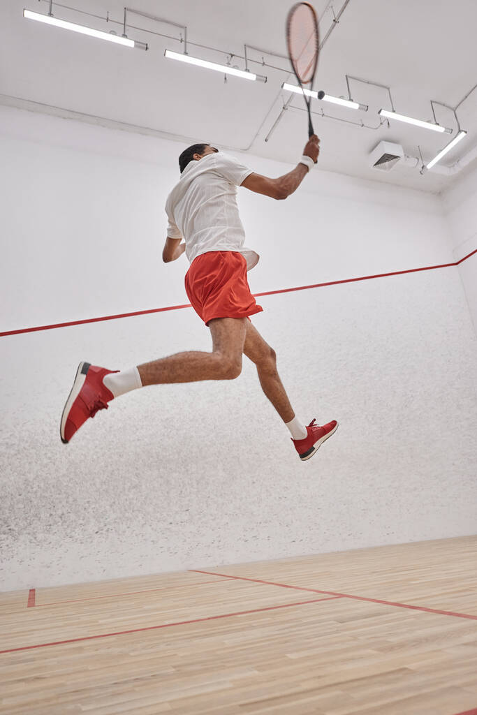 motion photo, attivo sportivo afroamericano che tiene la racchetta mentre salta e gioca a squash - Foto, immagini