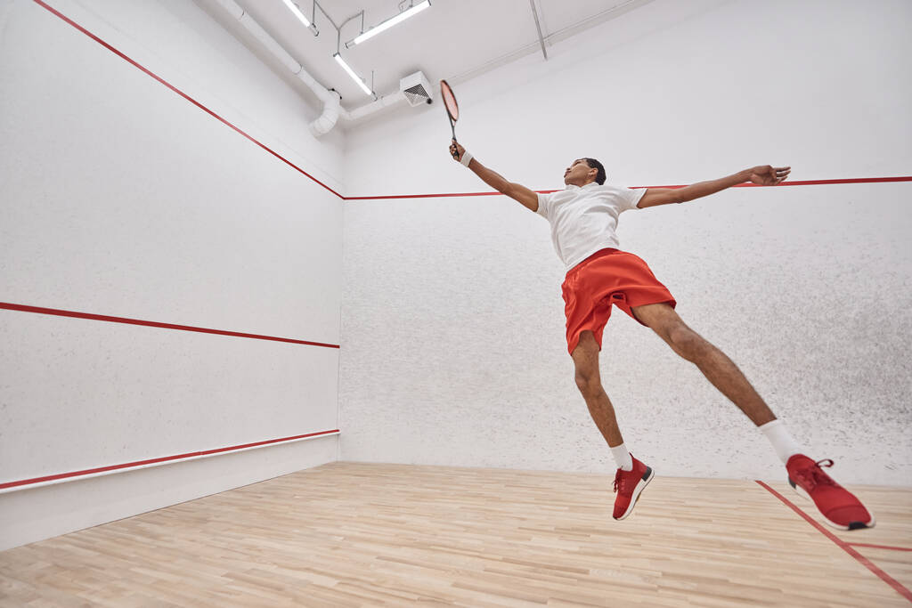 movimiento, enérgico deportista afroamericano con raqueta saltando y jugando squash en la corte - Foto, imagen