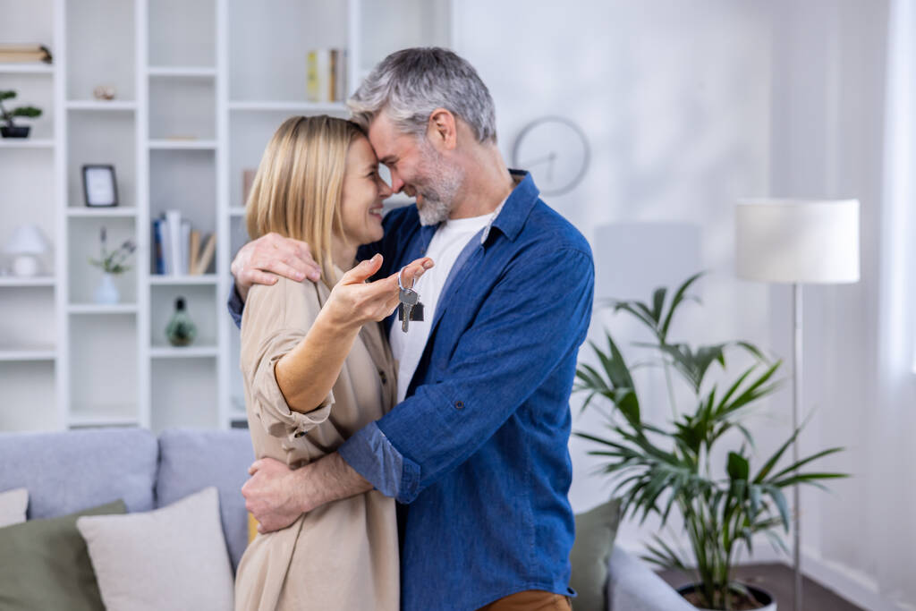 Ausgewählter Fokus, älteres grauhaariges Paar, Mann und Frau umarmen sich in neuem Wohnhaus, glückliche Familie hält Hausschlüssel. - Foto, Bild