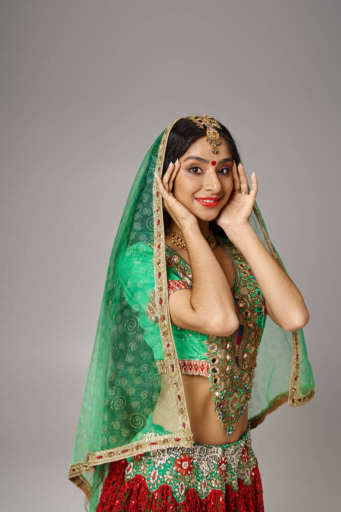 ελκυστική Ινδή γυναίκα σε εθνικά ρούχα με bindi και πέπλο κοιτάζοντας κάμερα, τα χέρια κοντά στο πρόσωπο - Φωτογραφία, εικόνα