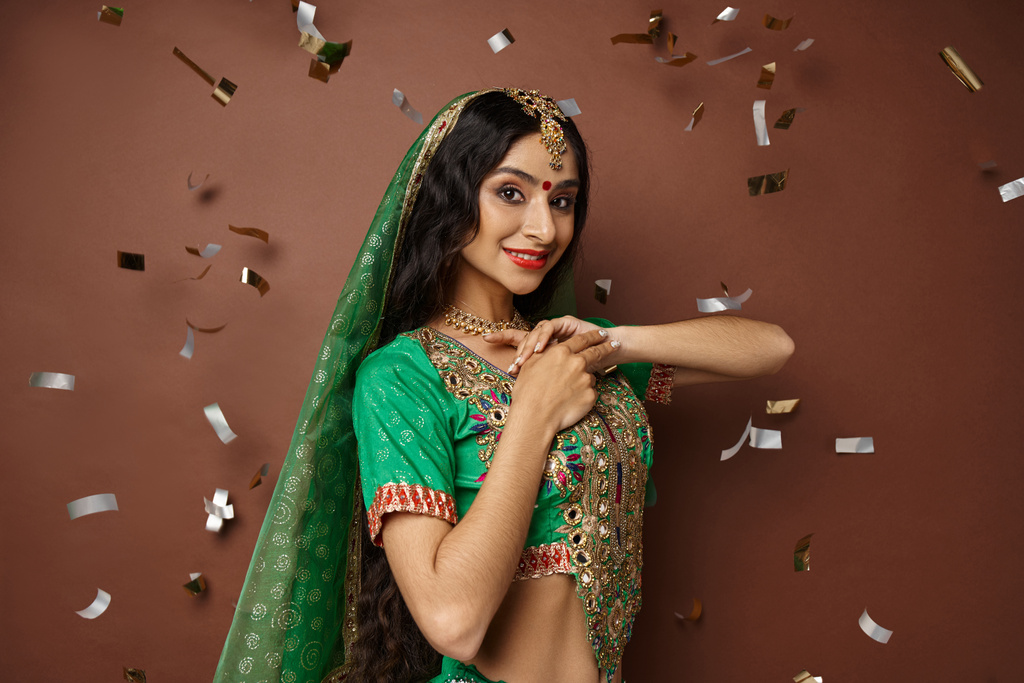 beautiful indian woman in green choli with red skirt with veil and bindi posing under confetti rain - Photo, Image