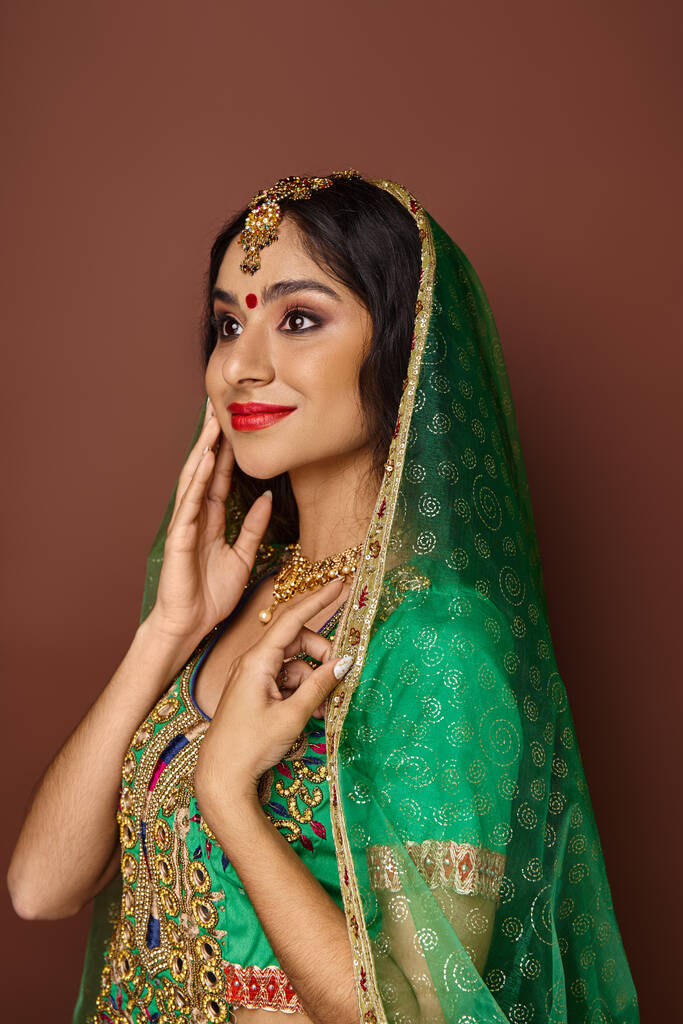 Geleneksel giyimli, elleri yanağında aksesuarlı neşeli Hintli kadının dikey çekimi. - Fotoğraf, Görsel
