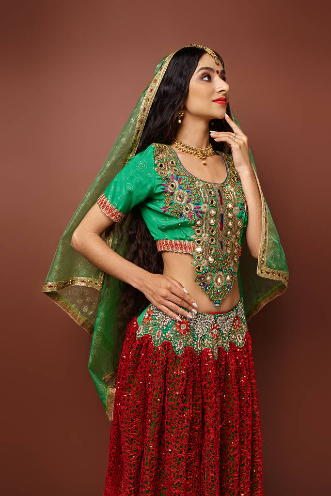 вертикальний знімок красивої індійської жінки в національному одязі з зеленою завісою позує рукою на стегні - Фото, зображення