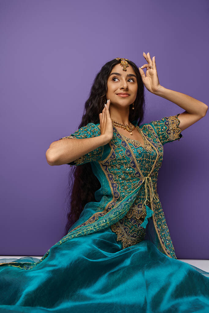 Ulusal kostüm giymiş, jest yapan ve yerde oturan güzel Hintli kadının dikey çekimi. - Fotoğraf, Görsel