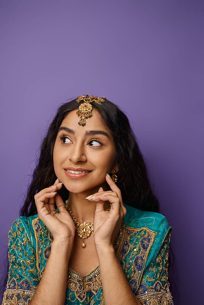 радісна молода індійська жінка в традиційному вбранні посміхається і дивиться в сторону руками біля туза - Фото, зображення