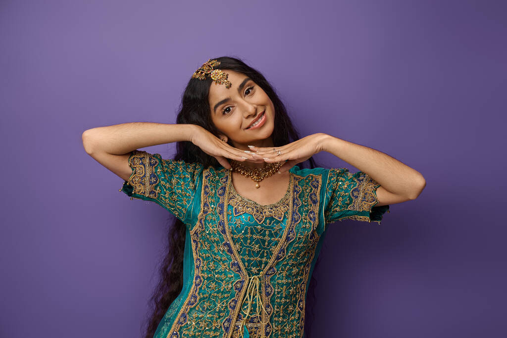 jolly aantrekkelijke indiaanse vrouw in nationaal kostuum poseren met de handen onder kin en glimlachen op de camera - Foto, afbeelding