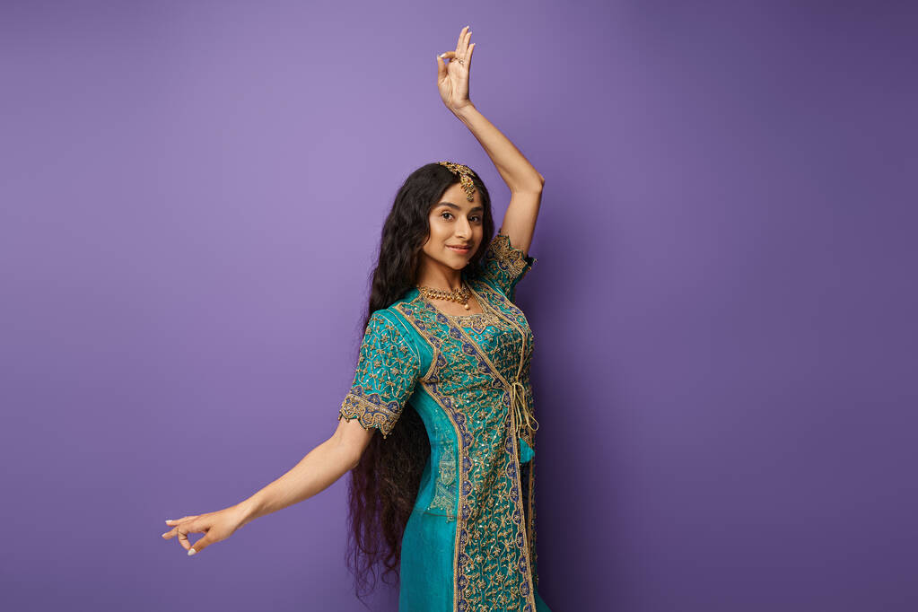 привлекательная индийская женщина в традиционном сари жестикулирует, танцуя и радостно улыбаясь в камеру - Фото, изображение