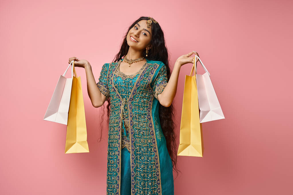 mulher indiana alegre em roupas tradicionais posando com sacos de compras e sorrindo alegremente para a câmera - Foto, Imagem