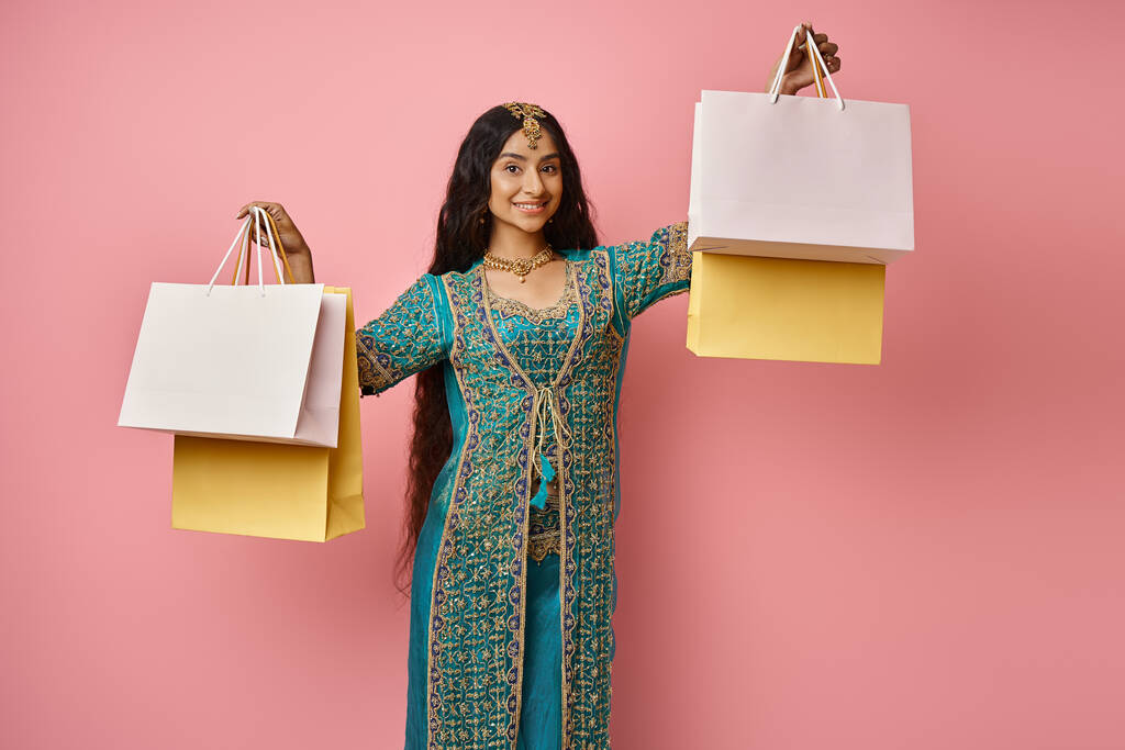 fröhliche indische Frau in traditionellem blauen Sari posiert mit Einkaufstüten in den Händen und lächelt in die Kamera - Foto, Bild