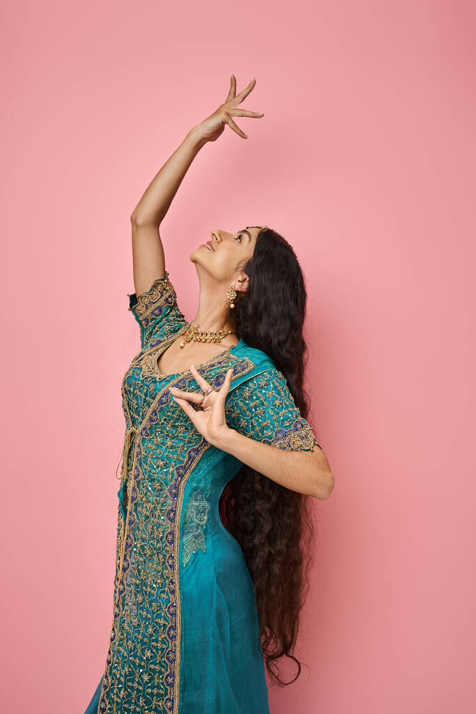 Mavi sari giymiş çekici Hintli bir kadının pembe arka planda dans ederken çekilmiş dikey çekimi. - Fotoğraf, Görsel