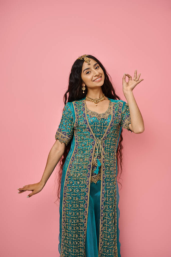 民族衣装のジェスチャーとピンクの背景にポーズで若いインドの女性の垂直ショット - 写真・画像