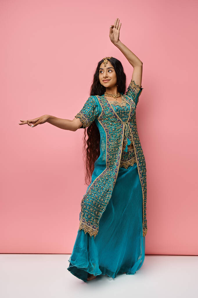 jovem mulher indiana atraente em gestos roupas nacionais enquanto dança em pano de fundo rosa - Foto, Imagem
