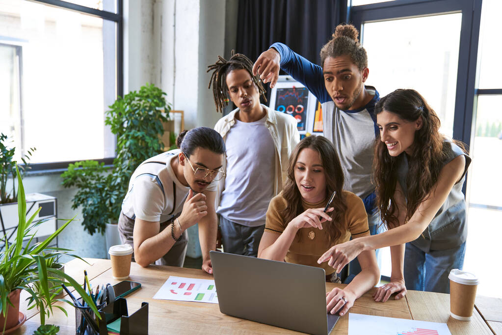 equipe multicultural surpreso e animado apontando para laptop perto de gráficos em mesa de trabalho, brainstorming - Foto, Imagem