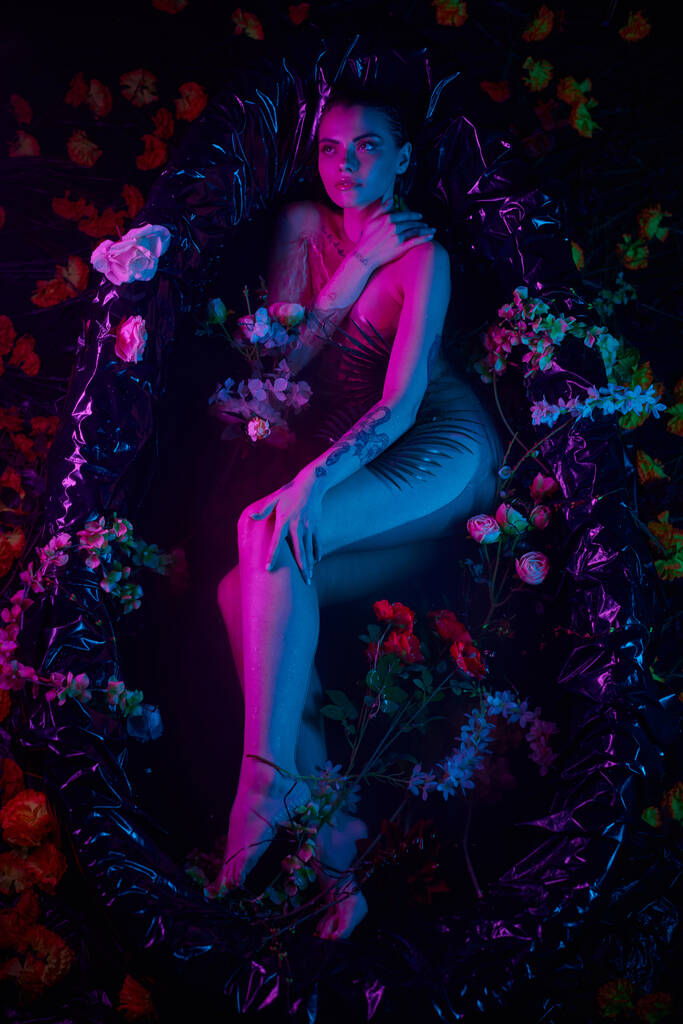 muoti laukaus, viehättävä nainen makaa keskuudessa palmunlehtiä ja kukkia kylpyammeessa, sininen ja violetti valot - Valokuva, kuva