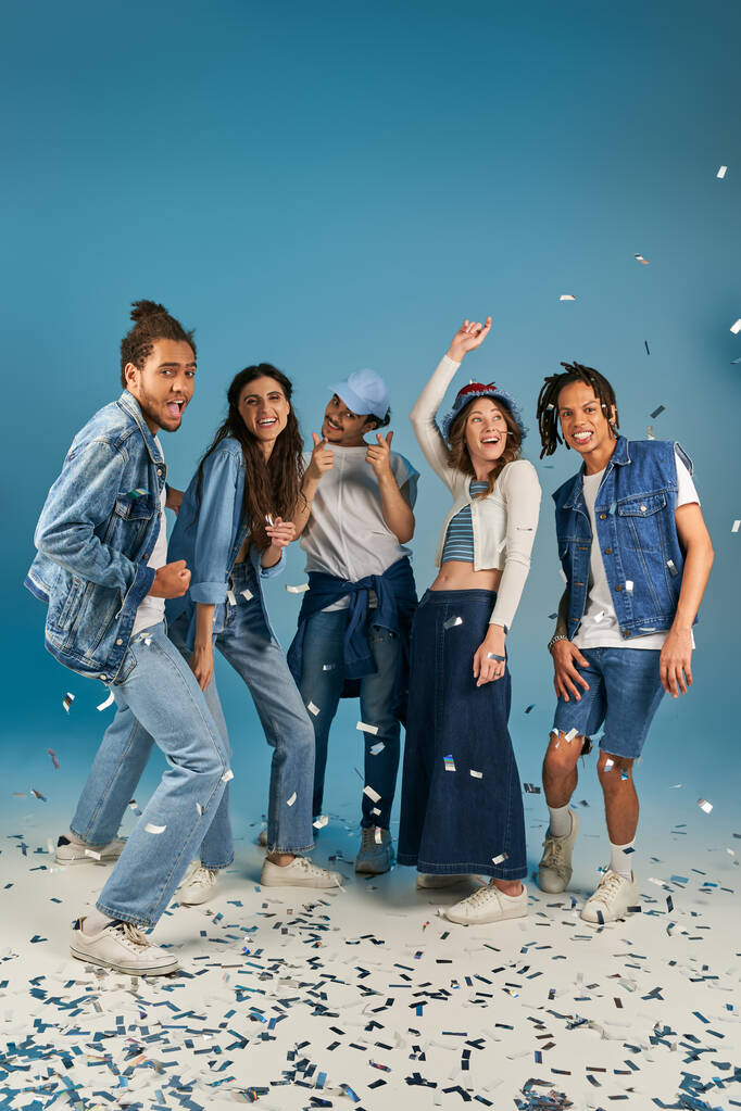 возбужденные многонациональные друзья в стильной повседневной одежде улыбаясь возле сверкающих конфетти, время вечеринки - Фото, изображение