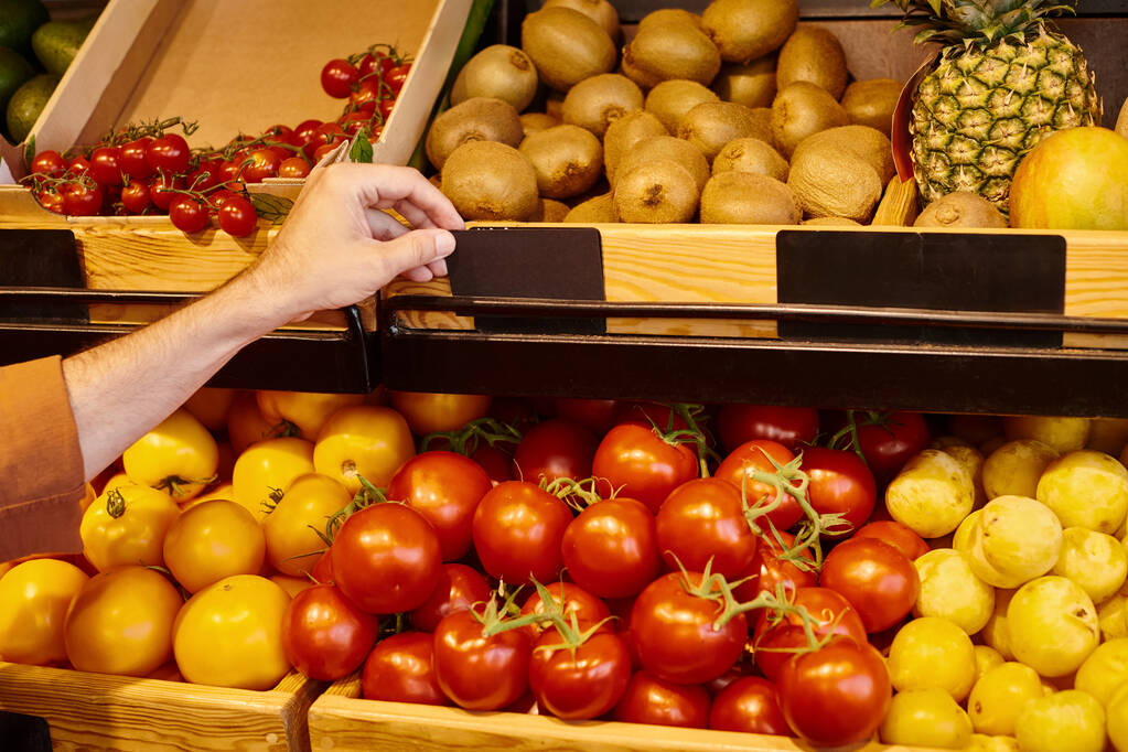 vista recortada de vendedor varón maduro poniendo precio etiqueta en el puesto de comestibles con frutas y verduras - Foto, imagen