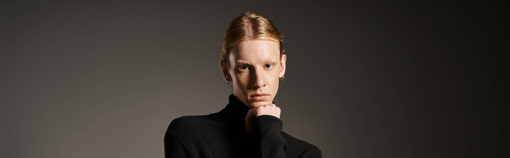 young non binary model in black turtleneck looking at camera with hand under chin, fashion, banner - Photo, Image