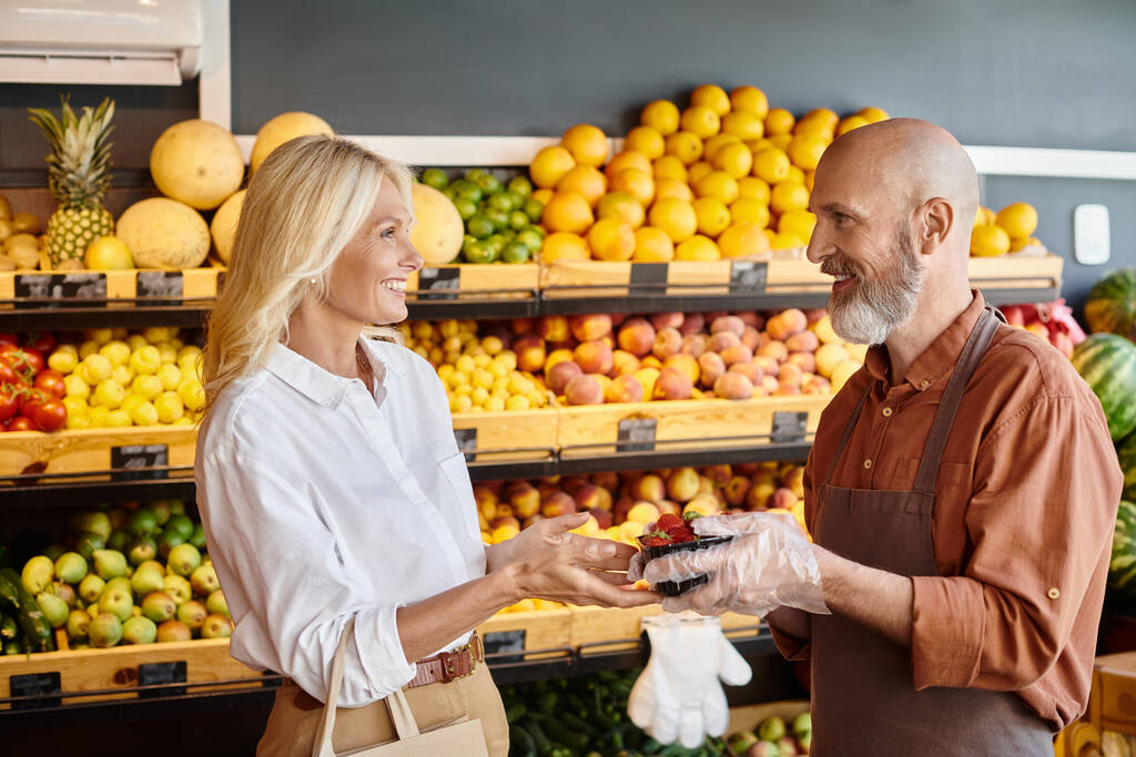 veselý vousatý prodejce dává balíček jahod svému veselému zákazníkovi, usmívá se jeden na druhého - Fotografie, Obrázek