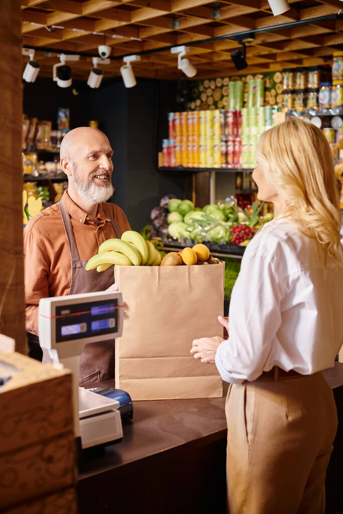 зрелый веселый продавец с бородой улыбаясь своему клиенту, что покупка свежих фруктов в продуктовом магазине - Фото, изображение