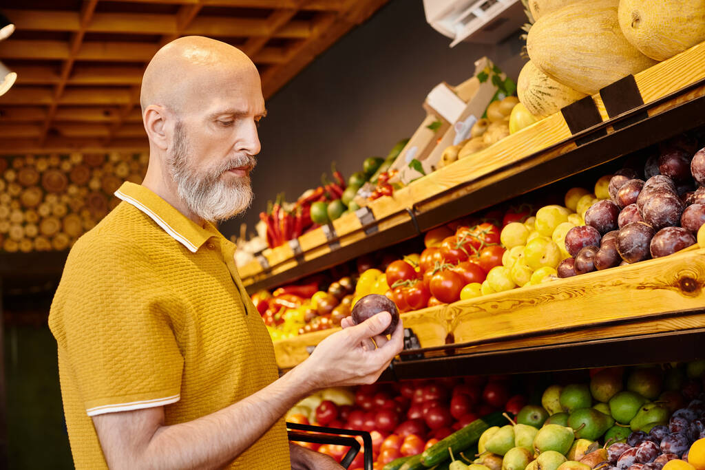 volwassen man in casual outfit met winkelmandje kiezen levendige sappige vruchten bij supermarkt - Foto, afbeelding