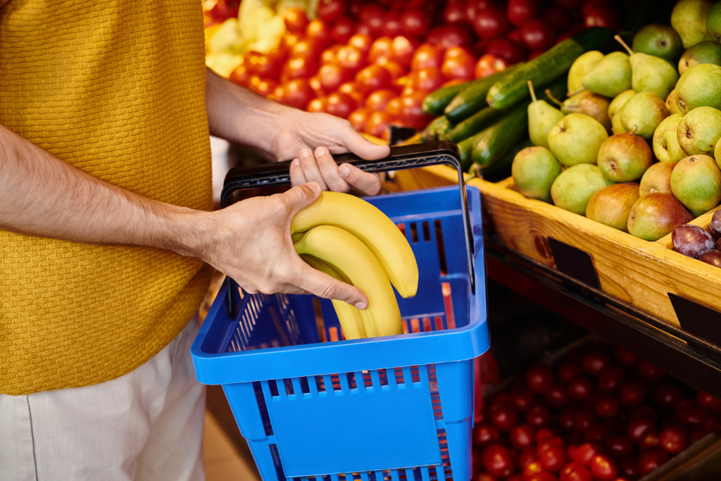 обрезанный вид зрелого мужчины клиента положить свежие бананы в корзину для покупок в продуктовом магазине - Фото, изображение