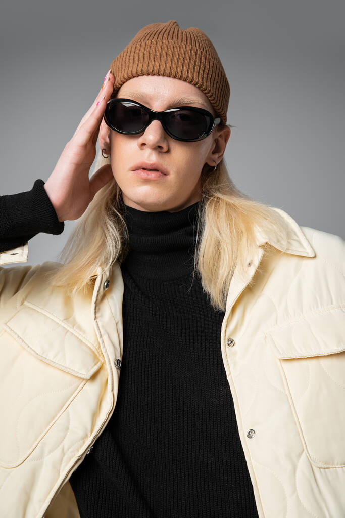 カメラを見ているサングラスと冬のトレンディなジャケットの若い非バイナリモデルの垂直ショット - 写真・画像