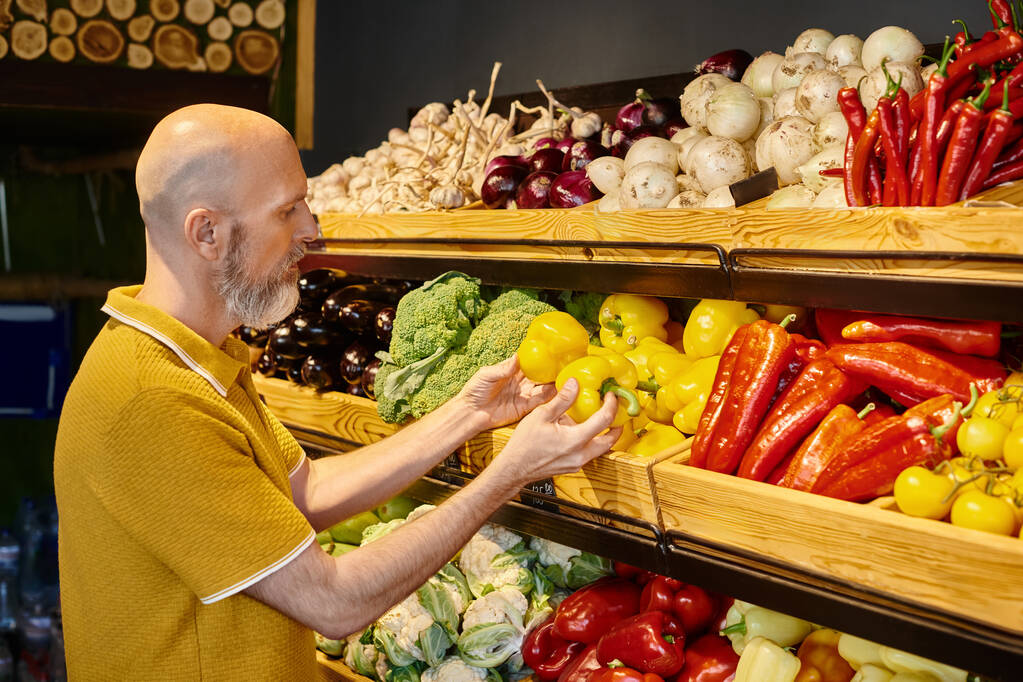 concentrated gray bearded man in casual attire choosing fresh vibrant peppers at grocery store - Photo, Image