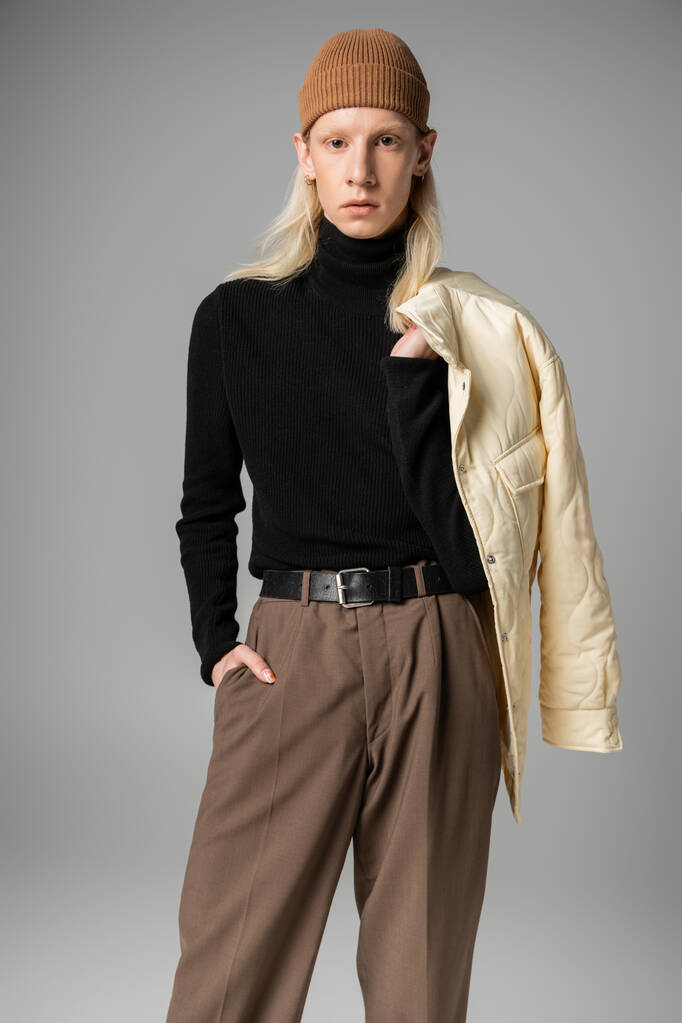 mladý stylový nebinární model pózující se zimní bundou a jednou rukou v kapse, módní koncept - Fotografie, Obrázek