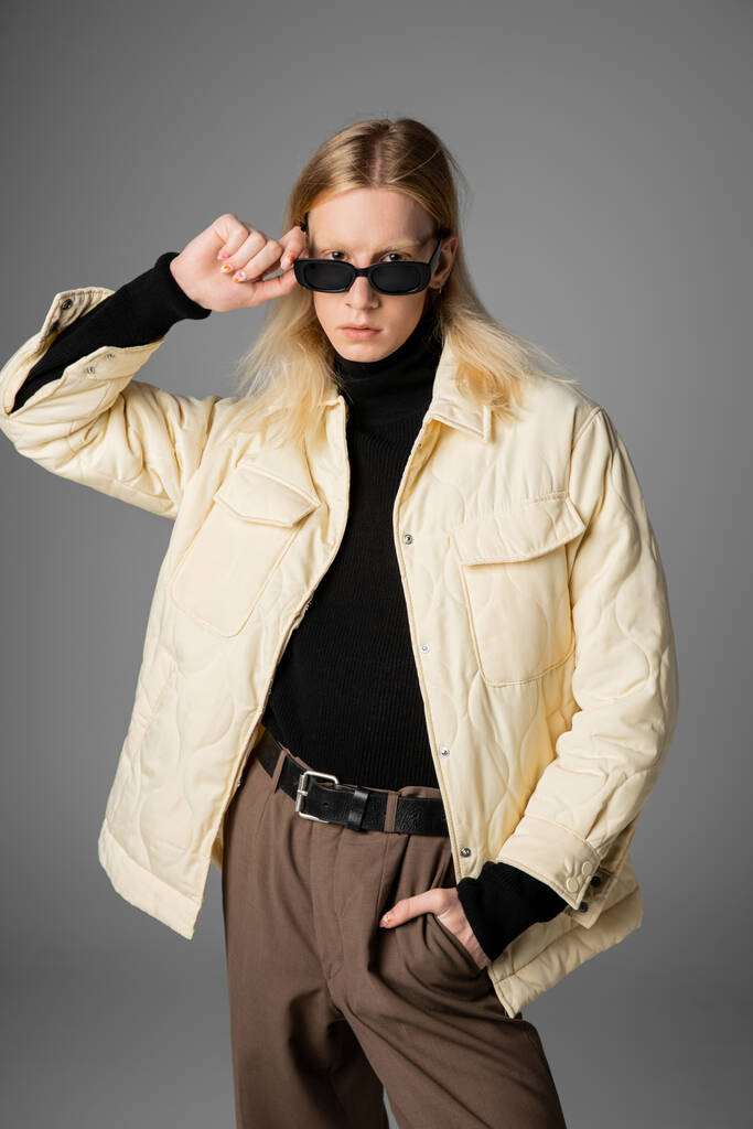 vertical shot of young androgynous person in warm stylish jacket touching glasses looking at camera - Photo, Image