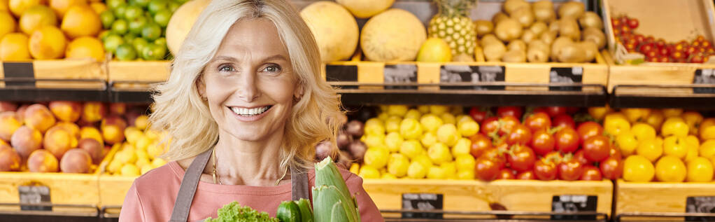 vidám érett eladó zöld mosolygó kamera gyümölcsök és zöldségek a háttérben, banner - Fotó, kép