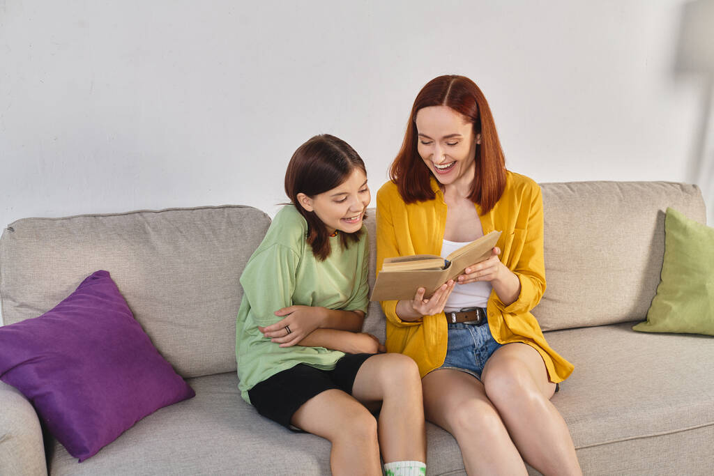mulher sorrindo ler livro sobre educação sexual para a filha adolescente no sofá acolhedor na sala de estar - Foto, Imagem