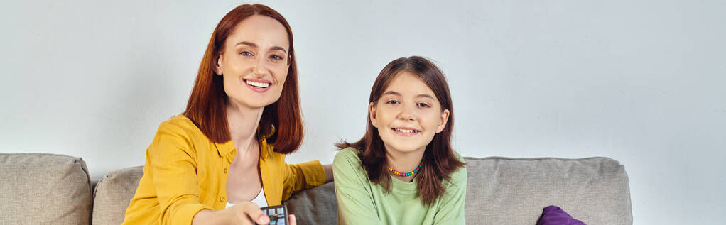 happy woman with remote controller watching tv with teenage daughter on sofa in living room, banner - Photo, Image