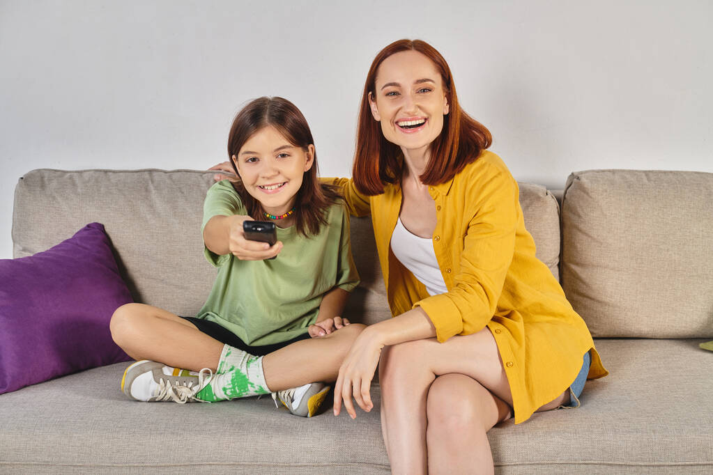 laughing woman with teenage daughter watching movie on cozy couch in modern living room, leisure - Photo, Image