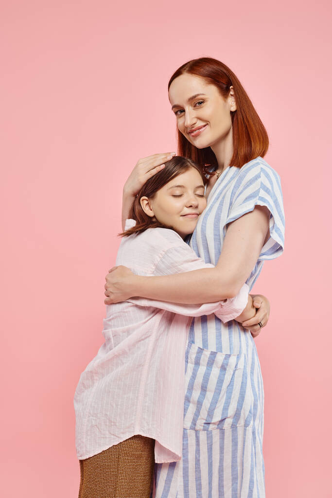 glücklich und trendy Frau umarmt Teenager-Tochter und lächelt in die Kamera auf rosa Hintergrund, Bonding - Foto, Bild