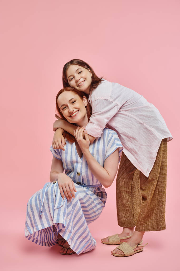 glückliches Teenagermädchen umarmt stilvolle Mutter posiert auf Verlockungen auf rosa Hintergrund, Liebe und Einheit - Foto, Bild