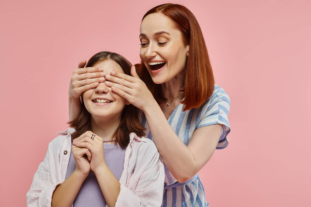 vrolijke en stijlvolle vrouw dekking ogen van tiener dochter tijdens het spelen raad eens wie spel op roze - Foto, afbeelding