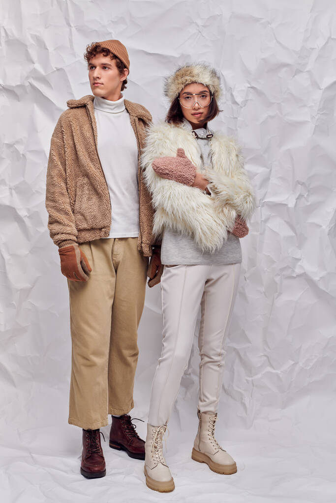 full length of multiethnic couple n fashionable winter attire on white crumpled paper backdrop - Photo, Image