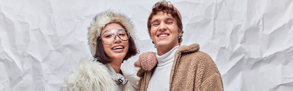 счастливая межрасовая пара в стильной зимней одежде глядя на камеру на белом текстурированном фоне, баннер - Фото, изображение