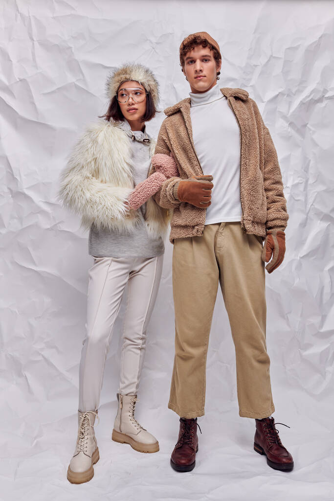 joven pareja interracial en traje de clima frío de pie sobre fondo de textura blanca, estilo de invierno - Foto, Imagen