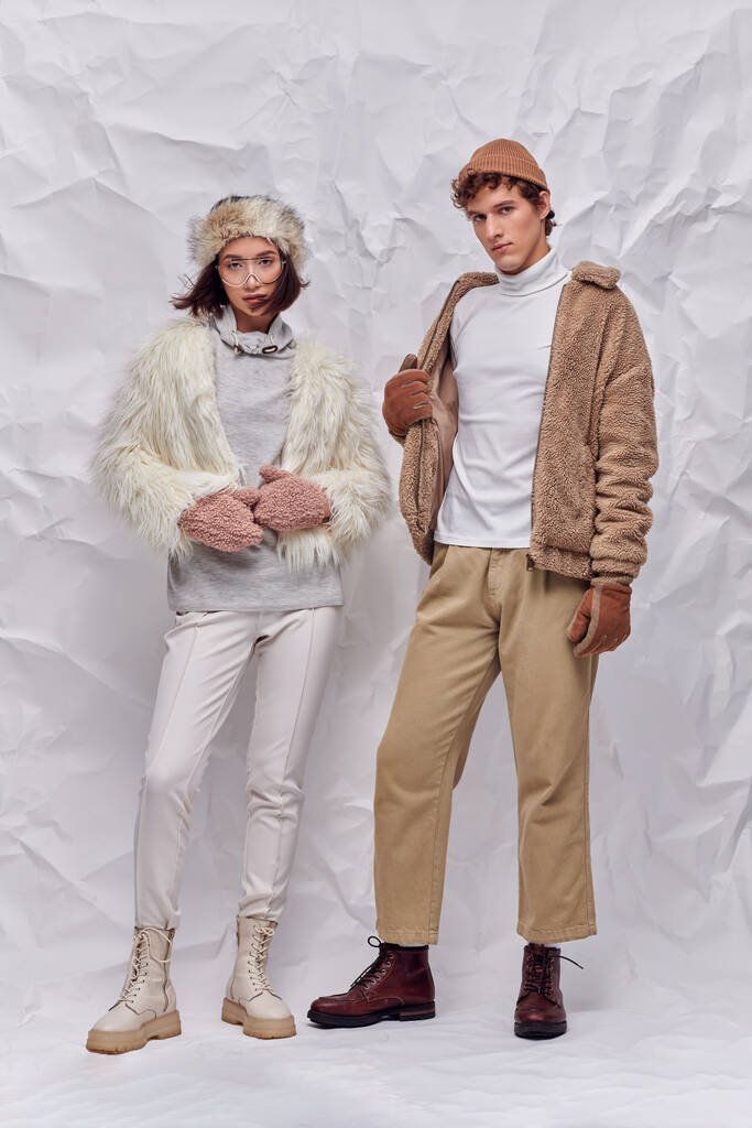 interracial couple in hats, warm gloves and faux fur jackets standing on white crumpled backdrop - Photo, Image