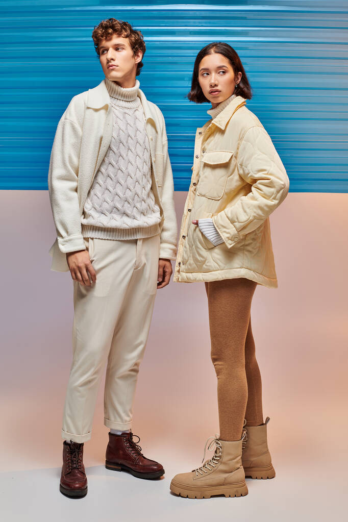 modelos multiétnicos en chaquetas calientes y botas de cuero cerca de lámina de plástico azul, moda de invierno - Foto, imagen