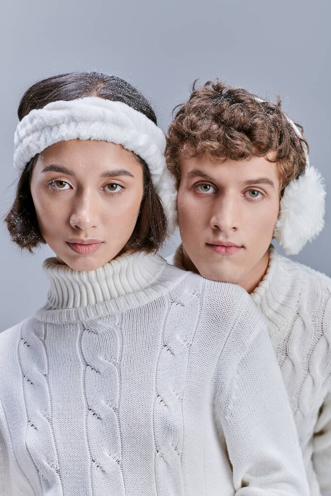 mladé mezirasové modely v teplém útulném oblečení při pohledu na kameru na šedé, zimní módní kampaň - Fotografie, Obrázek
