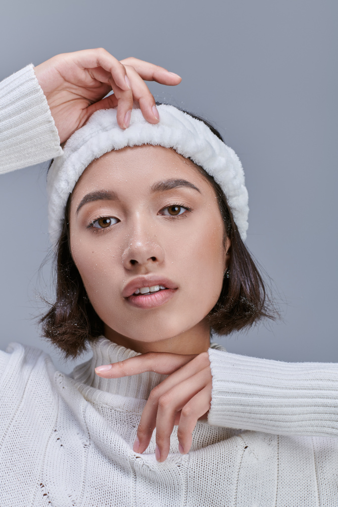 portrait of asian woman with snowy hair posing in white winter sweater and warm headband on grey - Photo, Image