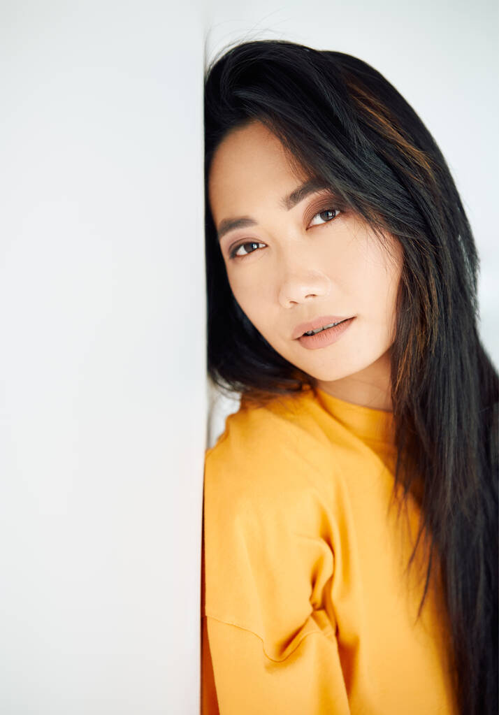 Hübsche sinnliche asiatische Frau in leuchtend gelbem T-Shirt posiert auf weißem Studiohintergrund. Weibliche Schönheit - Foto, Bild