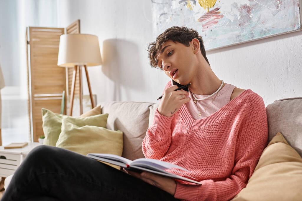 transgénero freelancer en jersey rosa hablando en smartphone y escribiendo en notebook en casa - Foto, imagen