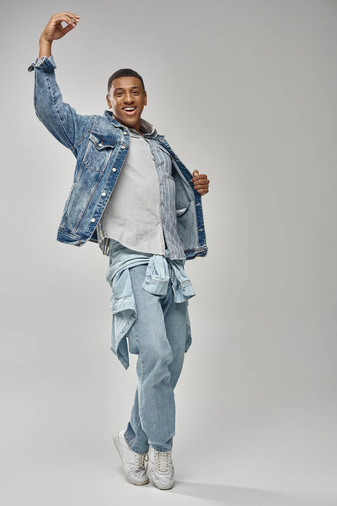 aantrekkelijke emotionele Afrikaanse Amerikaanse man in stijlvolle denim outfit gebaren levendige, mode concept - Foto, afbeelding