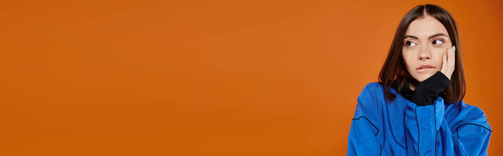 Burnu delinmiş, dudağını ısıran ve turuncu arka plana bakan düşünceli kadının bayrağı. - Fotoğraf, Görsel