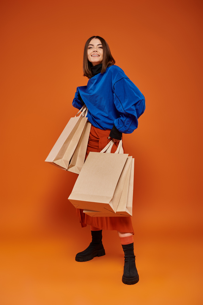 Aufgeregte Frau hält Einkaufstüten in der Hand und steht vor orangefarbenem Hintergrund, Verkaufskonzept für den Black Friday - Foto, Bild
