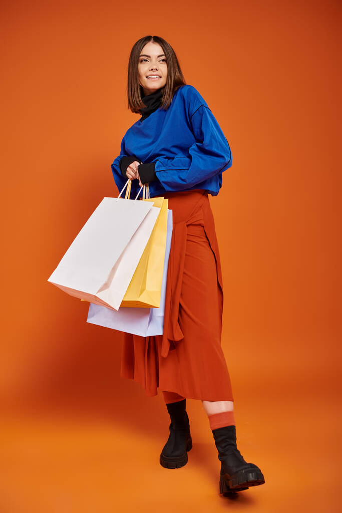 full length of cheerful woman in stylish autumnal clothes holding shopping bags on black friday - Photo, Image