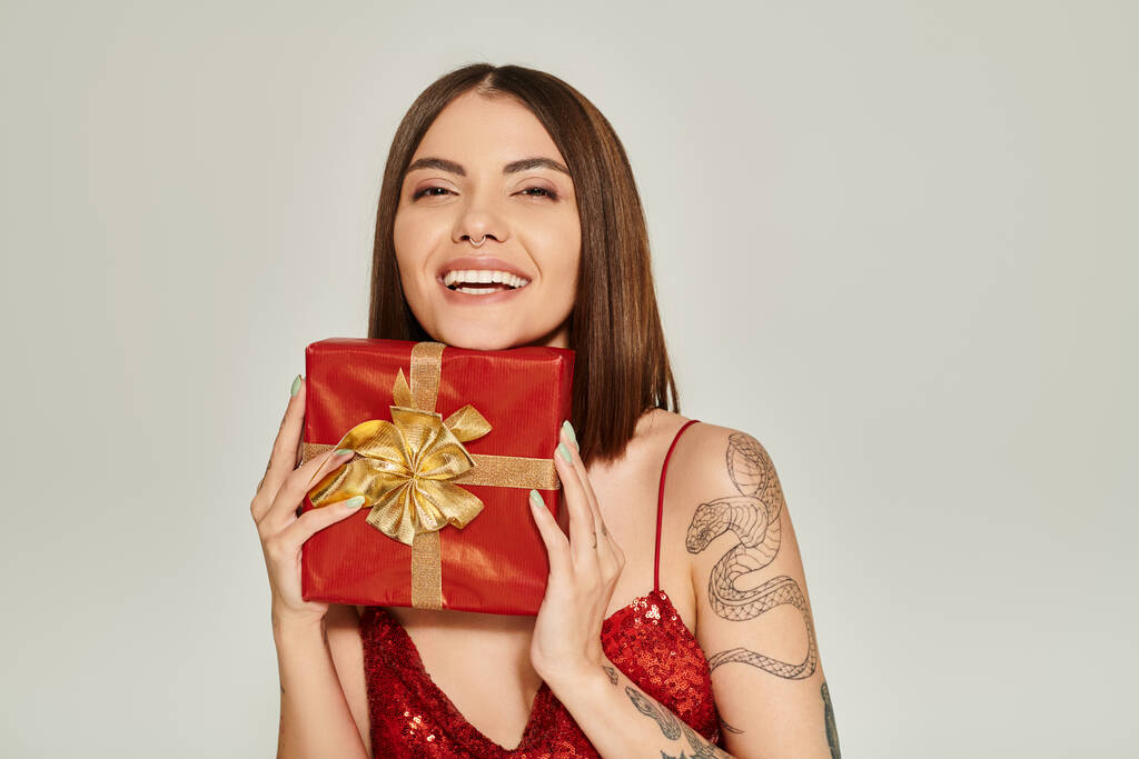 joyeuse jeune femme souriant sincèrement et tenant présent rouge dans les mains, concept de cadeaux de vacances - Photo, image